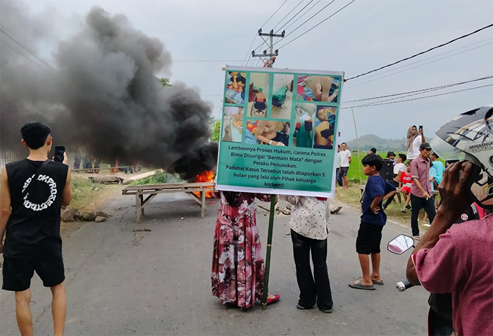 Ibu kandung korban penusukan memimpin aksi blokade jalan negara Lintas Bima-Sumbawa Jumat (20/6/2025) siang. Massa menuntut terduga pelaku penusukan pelajar ditangkap.